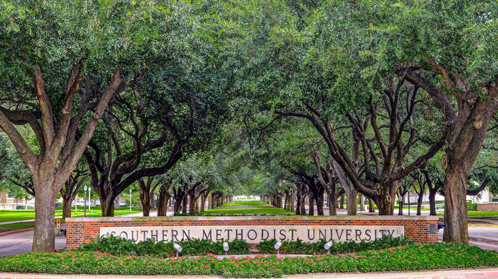 Sign of Southern Methodist University surrounded by trees & flowers.