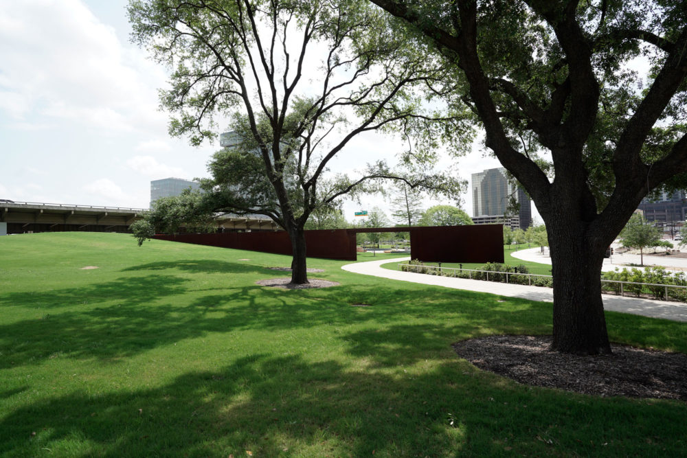 a grassy area with trees and a bridge in the background | Southern Botanical
