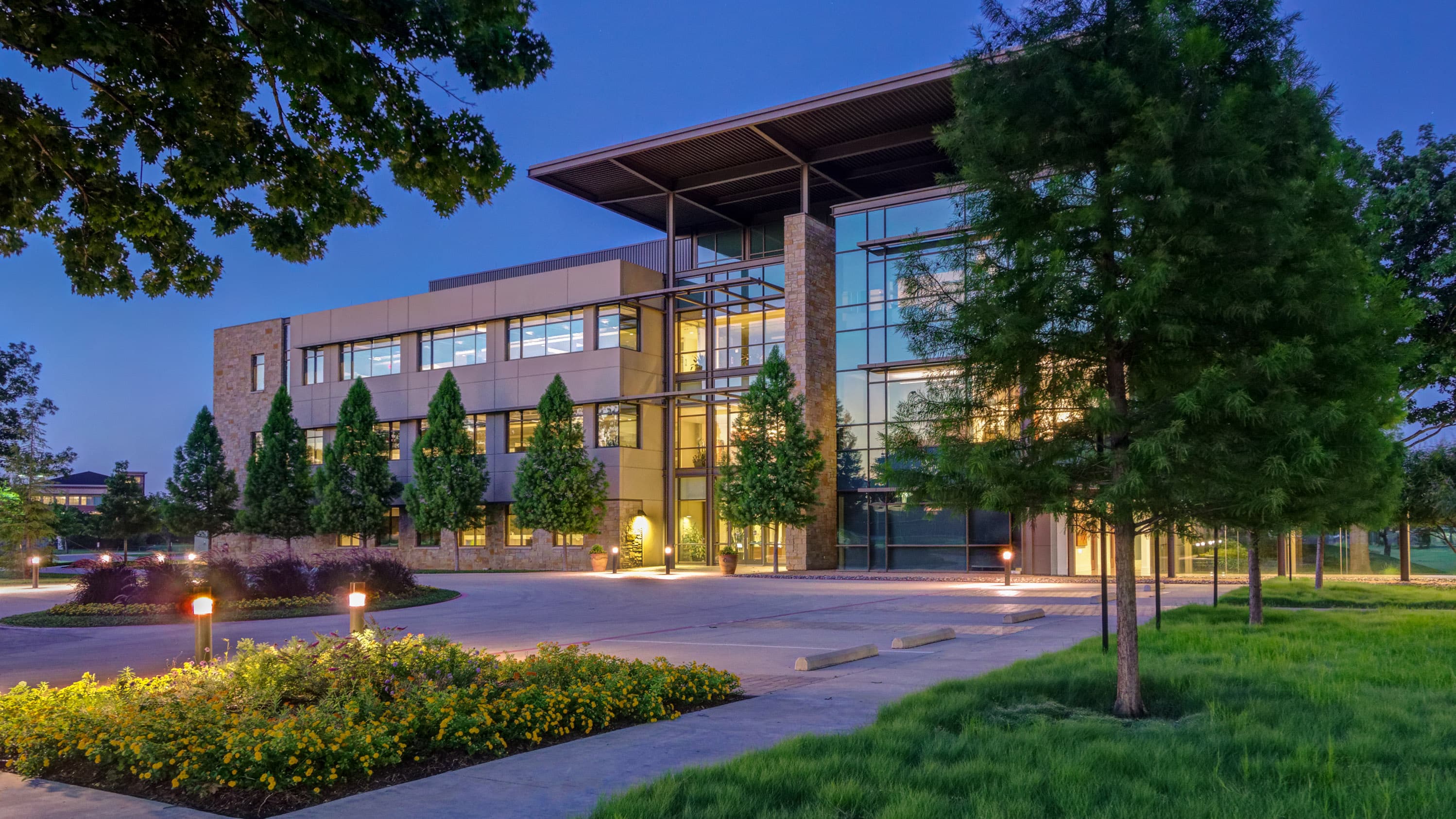 Evening shot of a modern corporate building in Texas with a custom landscape landscape design with outdoor lighting shining on the building, plants & trees.